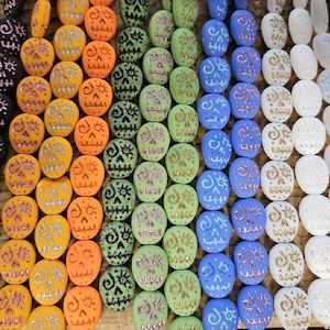 Puede incluir: Una colección de cuentas de calavera coloridas con diseños intrincados. Las cuentas están hechas de varios materiales, incluyendo cerámica, vidrio y madera. Las cuentas están enhebradas en una cuerda y están listas para ser utilizadas para la elaboración de joyas u otros proyectos de artesanía.