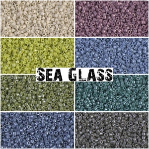 Könnte beinhalten: Sortiment kleiner, runder Glasperlen in verschiedenen Blautönen, Grüntönen und Violett. Die Perlen sind in einem Raster angeordnet und mit "SEA GLASS" beschriftet.
