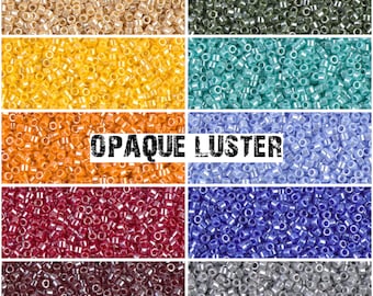 May include: Assortment of opaque luster seed beads in various colors, including beige, yellow, orange, light blue, lavender, blue, red, burgundy, and silver.  The beads are arranged in rows, with the text "OPAQUE LUSTER" printed across the middle.