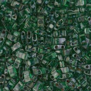 Puede incluir: Una vista de cerca muestra un montón de pequeñas cuentas verdes rectangulares. Las cuentas tienen una cualidad translúcida, con una mezcla de secciones sólidas y transparentes. Las cuentas están dispersas, creando una superficie texturizada e irregular.