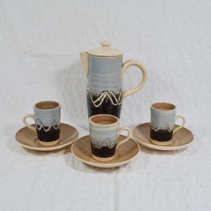 May include: A ceramic coffee set. It includes a tall coffee pot with a lid, and three matching coffee cups with saucers. The set has a blue, brown, and cream colour scheme with a wavy design.