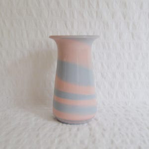 May include: A decorative vase with a flared top and a rounded base. The vase features horizontal stripes of soft pink and grey-blue. The vase is made of ceramic or glass and is suitable for displaying flowers or as a decorative accent.