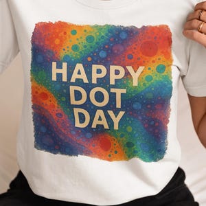 May include: White t-shirt with a colorful, abstract design featuring the words "HAPPY DOT DAY" in a bold font. The design incorporates a spectrum of colors, including red, orange, yellow, green, blue, and purple.