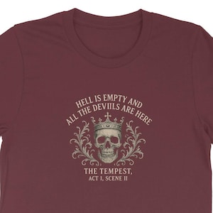 Puede incluir: Camiseta burdeos con un cráneo coronado rodeado de adornos. El texto dice "HELL IS EMPTY AND ALL THE DEVILS ARE HERE" y "THE TEMPEST, ACT 1, SCENE II".