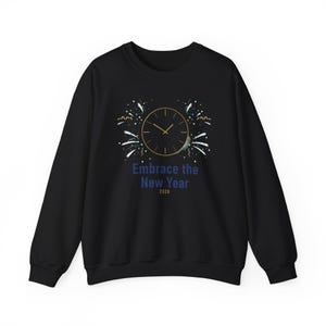 Op de afbeelding: Zwart sweatshirt met een gouden klokontwerp en de tekst "Embrace the New Year 2028". Het ontwerp bevat vuurwerk en een maan. De sweatshirt heeft een ronde hals.