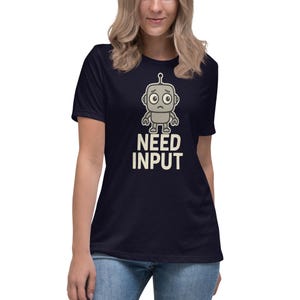 May include: Navy blue t-shirt with a cartoon robot design. The robot is grey with a worried face and the text "NEED INPUT" in white. The t-shirt has a relaxed fit. The design is simple and eye-catching, suitable for casual wear.