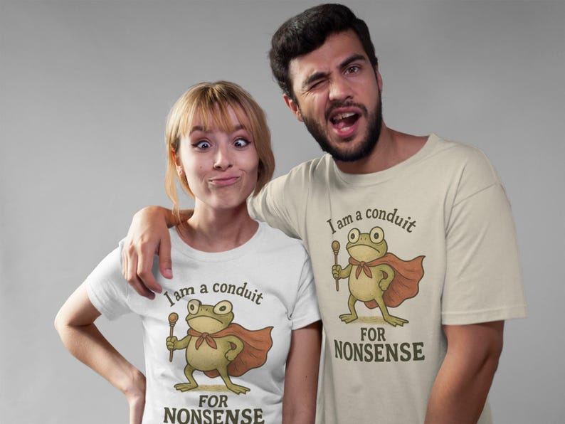 Peut inclure: Deux personnes portant des t-shirts assortis avec un dessin de grenouille. La grenouille, portant une cape et tenant un b&acirc;ton, est imprim&eacute;e avec le texte "I am a conduit FOR NONSENSE". Les chemises sont blanches et beiges.