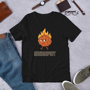 May include: Black t-shirt featuring a cartoon brain with flames and the word "NEUROSPICY" in a gold color. The brain has a smiling face and is walking. The shirt is made of a soft material.