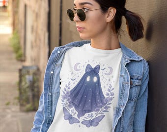 May include: White t-shirt with a whimsical ghost design. The ghost is draped in a blue sheet with a bow, surrounded by butterflies, flowers, and celestial elements. The design is centered on the shirt.