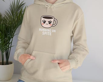 Könnte beinhalten: Beiger Kapuzenpullover mit Fronttasche und Kordelzugkapuze. Auf der Vorderseite befindet sich eine Grafik einer wütenden Kaffeetasse mit dem weißen Text "RUNNING ON SPITE". Der Hoodie ist aus weichem Material.