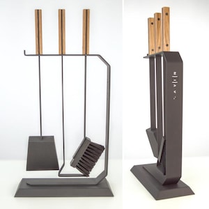 Puede incluir: Un juego de herramientas para chimenea de color gris oscuro con mangos de madera. El juego incluye una pala, un cepillo y un atizador, todo sostenido por un soporte a juego. Los mangos son de color marrón claro con una raya oscura. La palabra "AVEN" está impresa en el soporte.