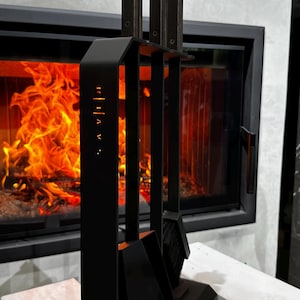 May include: A black fireplace tool set with a stand. The set includes a poker, shovel, and brush. The tools are displayed in front of a fireplace with a bright orange flame.