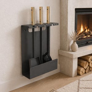 Pode incluir: Um conjunto de ferramentas para lareira preto fosco com três ferramentas, uma escova e uma pequena pá. As ferramentas têm cabos de madeira clara. O conjunto é montado numa parede perto de uma lareira com fogo e um vaso de flores secas.