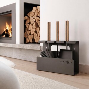 Pode incluir: Um conjunto de ferramentas para lareira em metal cinzento-escuro mate com um suporte de parede que apresenta o texto SAVEN impresso na frente. O conjunto inclui três ferramentas com cabos de madeira castanho-claro, uma escova preta e uma pá de metal preta.