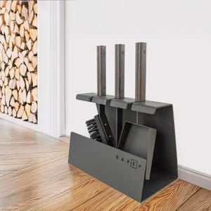 Peut inclure: Un ensemble d'outils de cheminée gris foncé comprenant une pelle, une brosse et un tisonnier. L'ensemble comprend un support avec trois poteaux verticaux et le mot "SAVEN" imprimé sur le devant. Les outils sont exposés sur un sol en bois.
