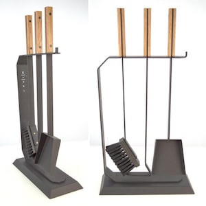 Könnte beinhalten: Ein dunkelgraues Kaminwerkzeug-Set mit Holzgriffen. Das Set enthält einen Schürhaken, eine Schaufel, eine Bürste und einen Ständer. Die Griffe sind hellbraun mit einem dunkelbraunen Streifen. Der Ständer hat ein modernes Design.