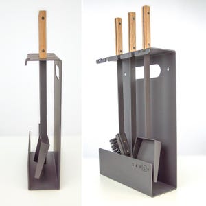 Könnte beinhalten: Ein dunkelgraues Kaminwerkzeug-Set mit Holzgriffen. Das Set enthält einen Schürhaken, eine Schaufel, eine Bürste und einen Ständer mit dem Wort "SAVEN" auf der Vorderseite. Die Werkzeuge sind ordentlich im Ständer angeordnet.