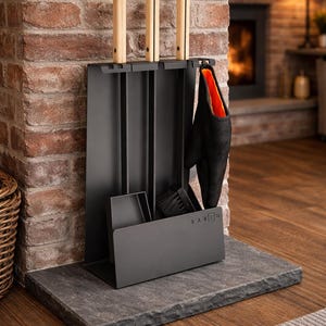 Puede incluir: Un juego de herramientas para chimenea negro con mangos de madera y un soporte a juego. El juego incluye un cepillo, una pala y un atizador, con un guante negro con interior naranja colgado a un lado. Las herramientas se exhiben sobre un hogar de piedra.