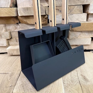 Könnte beinhalten: Ein schwarzes Metall-Kaminwerkzeug-Set mit Schaufel, Bürste und Schürhaken. Die Werkzeuge haben helle Holzgriffe mit einem schwarzen Streifen. Das Set enthält das Wort "AVEN" an der Seite.