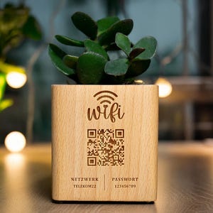 Könnte beinhalten: Ein Holzpflanzgefäß mit einer Sukkulentenpflanze. Auf dem Pflanzgefäß sind das Wort "wifi" und ein QR-Code eingraviert. Unter dem QR-Code stehen die Wörter "NETZWERK TELEKOM22" und "PASSWORT 123456789".