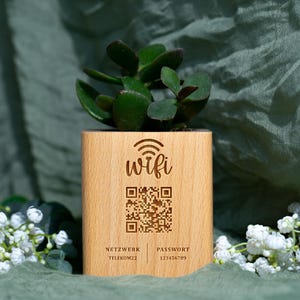 May include: A wooden planter with a succulent plant. The planter has the word "wifi" and a QR code engraved on the front. Below the QR code are the words "NETZWERK" and "PASSWORT" with corresponding information.