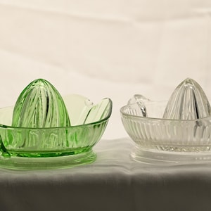May include: Two glass citrus juicers. One is a vibrant green, the other is clear. Each has a ridged bowl and a conical reamer. The green juicer has a handle. These vintage kitchen tools are ideal for squeezing fresh juice.