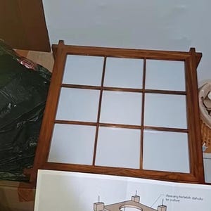 Könnte beinhalten: Ein quadratischer Holzrahmen mit neun weißen Paneelen. Der Rahmen ist dunkelbraun. Im Vordergrund befindet sich eine Zeichnung mit Text, die zeigt, wie der Rahmen installiert wird.