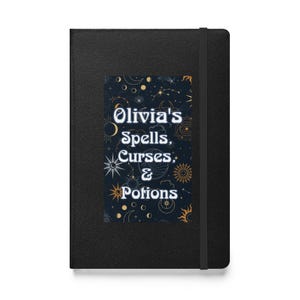 Puede incluir: Cuaderno negro con el texto "Olivia's Spells, Curses, & Potions" sobre un fondo azul oscuro con ilustraciones celestiales. El cuaderno tiene un cierre de banda elástica.