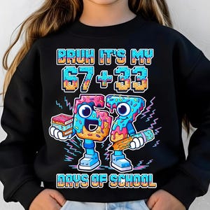 以下が含まれることがあります： 「BRUH IT'S MY 67 + 33 DAYS OF SCHOOL」と書かれたカラフルなグラフィックが特徴の黒いスウェットシャツ。グラフィックは、顔のあるドーナツに似たアニメーション数字で、本と鉛筆を持っています。