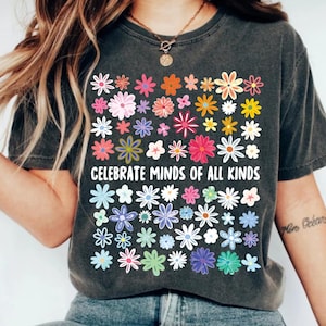 May include: Dark gray t-shirt featuring a colorful floral design with the text "CELEBRATE MINDS OF ALL KINDS". The flowers are in various colors, including pink, orange, blue, and green. The shirt has a vintage, worn look.