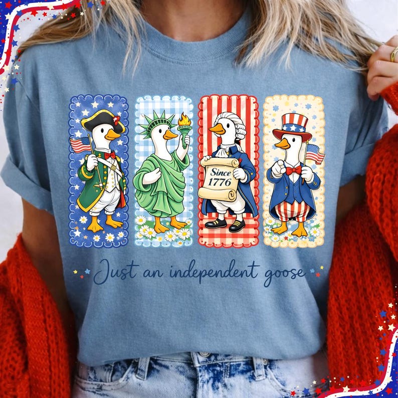 May include: Light blue t-shirt featuring four cartoon geese dressed in patriotic attire. The geese are depicted as historical figures, including a soldier, the Statue of Liberty, a founding father, and Uncle Sam. The text "Just an independent goose" is below.