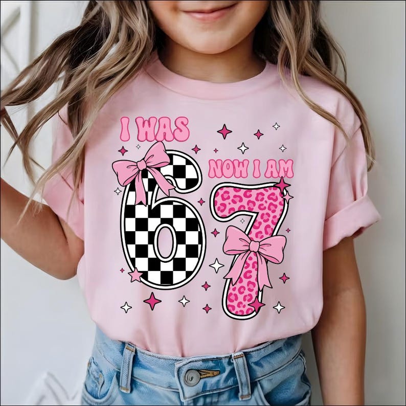 May include: A pink t-shirt with the text "I WAS 6 NOW I AM 7". The number 6 is black and white checkered, and the number 7 is pink leopard print. Pink bows and stars decorate the shirt.