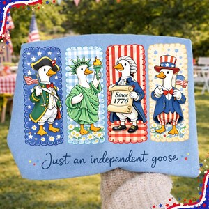 May include: Light blue decorative pillow featuring four cartoon geese dressed in patriotic attire. Each goose represents a different historical figure, holding flags and scrolls. The text "Just an independent goose" is written across the bottom.