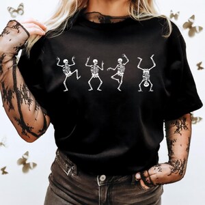 Pu&ograve; includere: T-shirt nero con grafica bianca di scheletri danzanti. Gli scheletri sono in varie pose, con braccia e gambe distese. La maglietta ha un girocollo e maniche corte. Il disegno &egrave; centrato sul davanti della maglietta.