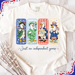 May include: Cream-colored t-shirt featuring four cartoon geese dressed in patriotic attire. Each goose is in a different frame with a blue, red, or white background. The text "Just an independent goose" is printed below the geese.