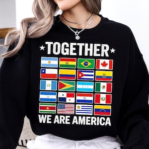 May include: Black sweatshirt with the words "TOGETHER" and "WE ARE AMERICA" in white. The design features a grid of flags from various countries in the Americas, including the United States, Canada, and Brazil.