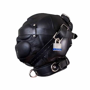 Könnte beinhalten: Schwarze Lederhaube mit gepolstertem Maul und einer Reihe von Riemen und Schnallen. Ein silbernes Vorhängeschloss sichert die Haube, die auch einen Metallring an der Basis aufweist.