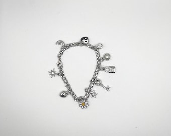 May include: Silver charm bracelet featuring various charms, including a yin-yang symbol, a lock, a key, a daisy, and stars. The bracelet is made of a chain link design and is displayed on a white background.