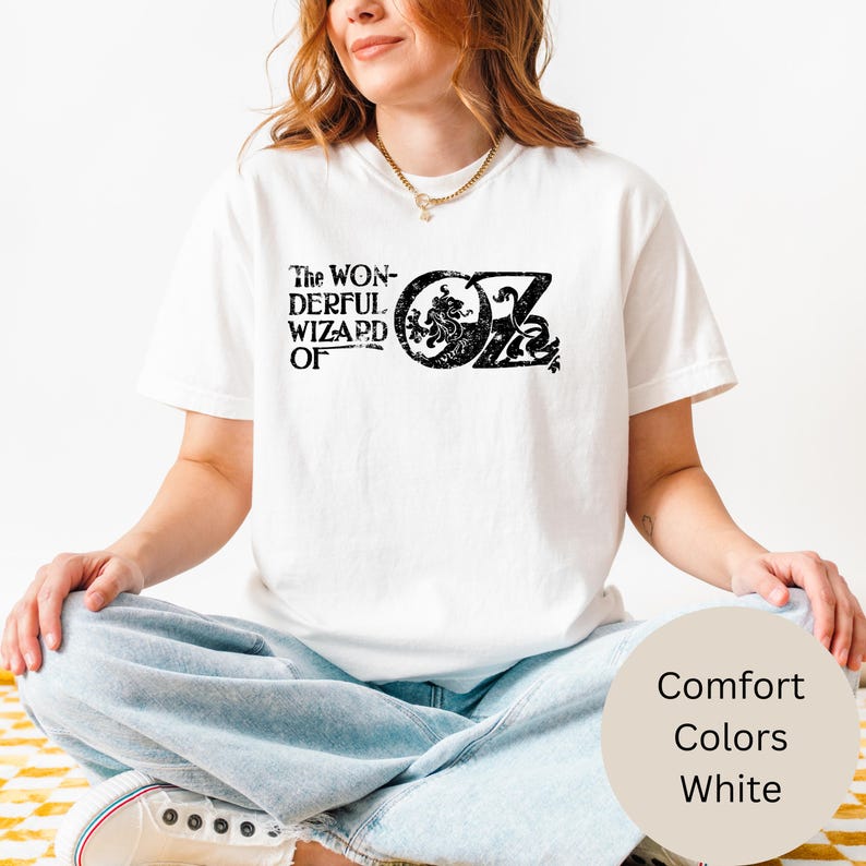 以下が含まれることがあります： 「The Wonderful Wizard of Oz」の黒い文字がプリントされた白いTシャツ。 デザインには、装飾的な要素を持つ象徴的な「OZ」ロゴが含まれています。 このシャツは「Comfort Colors」コレクションの一部です。