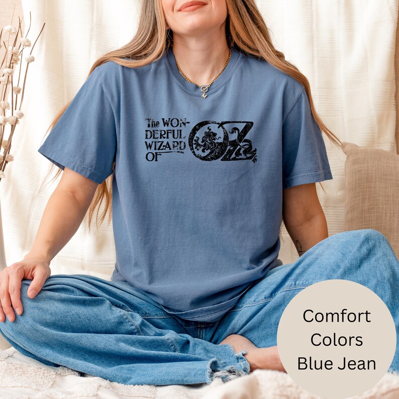 May include: A blue t-shirt featuring the text "The Wonderful Wizard of Oz" in black. The shirt is a comfort colour and is blue jean in colour.