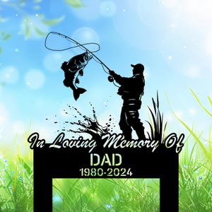 May include: Black metal memorial sign with a silhouette of a fisherman catching a fish. The sign reads "In Loving Memory Of DAD 1980-2024" against a blue sky and green grass background. A touching tribute.