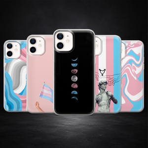 Puede incluir: Una colección de fundas para teléfonos con varios diseños. Una funda presenta un fondo negro con un diseño de fases lunares. Otras fundas muestran una bandera transgénero, un patrón similar al mármol y una estatua con un símbolo transgénero.