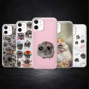 May include: A collection of phone cases with various hamster-themed designs. One case is pink with a hamster wearing a pink bow. Other cases feature hamsters with different accessories and text. The cases are displayed against a dark background.