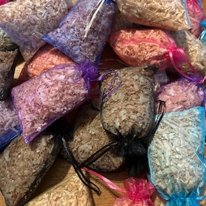 May include: A collection of small, mesh bags filled with wood shavings. The bags are tied with colorful ribbons in shades of pink, blue, purple, and black. The wood shavings are various shades of brown and tan.