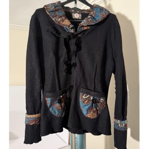 May include: Black jacket with a decorative paisley pattern on the collar, pockets, and cuffs. The jacket has a button-up front, two front pockets, and long sleeves. The paisley pattern includes shades of blue, brown, and gold.