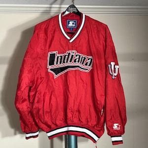 May include: A red Starter Indiana Hoosiers jacket with a white and black design. The jacket has a V-neck collar with white trim and the word "Indiana" across the chest. The Indiana University logo is on the sleeve.