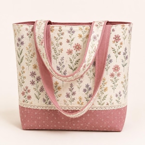 Peut inclure: Un sac fourre-tout en tissu crème orné d'un motif floral de fleurs sauvages roses, jaunes et violettes. La partie inférieure est en tissu rose poudré uni avec un motif de petits points blancs, séparée par une fine bordure en dentelle crème.