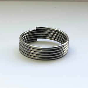 Peut inclure: Une bague argentée au design unique. La bague est composée de plusieurs bandes parallèles, étroitement enroulées, créant un effet de superposition. Les bandes sont lisses et ont un éclat métallique. C'est un bijou simple mais moderne.