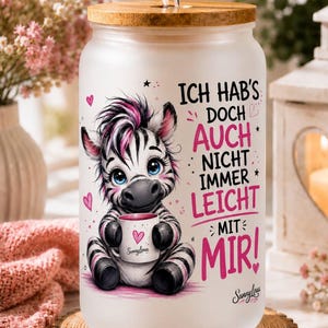 Könnte beinhalten: Ein mattiertes Glas mit Bambusdeckel und klarem Glasstrohhalm. Das Motiv zeigt ein Zebrababy, das eine kleine Tasse hält, umgeben von rosa Herzen und Sternen. Der Text lautet: ICH HAB'S DOCH AUCH NICHT IMMER LEICHT MIT MIR! und SunnyLou.