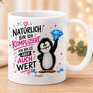 Könnte beinhalten: Eine weiße Keramiktasse mit einem Cartoon-Pinguin, der einen blauen Diamanten hält. Der Text lautet: Naturlich bin ich kompliziert, ich bin es aber auch wert. Das Design enthält rosa Herzen, blaue Sternakzente und den Markennamen Sunny Lou.